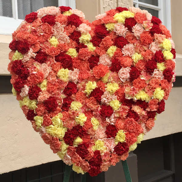 Heart-shaped floral arrangement of red, pink, peach, and yellow carnations