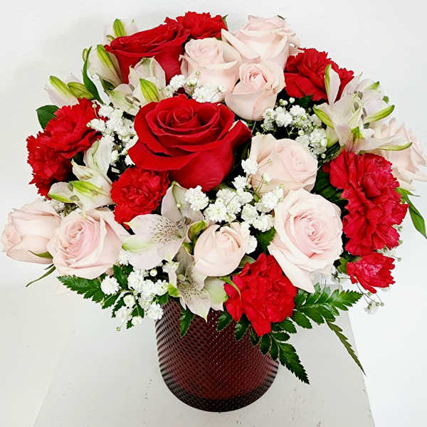 Bouquet of red and pale pink roses with white filler flowers in a dark vase