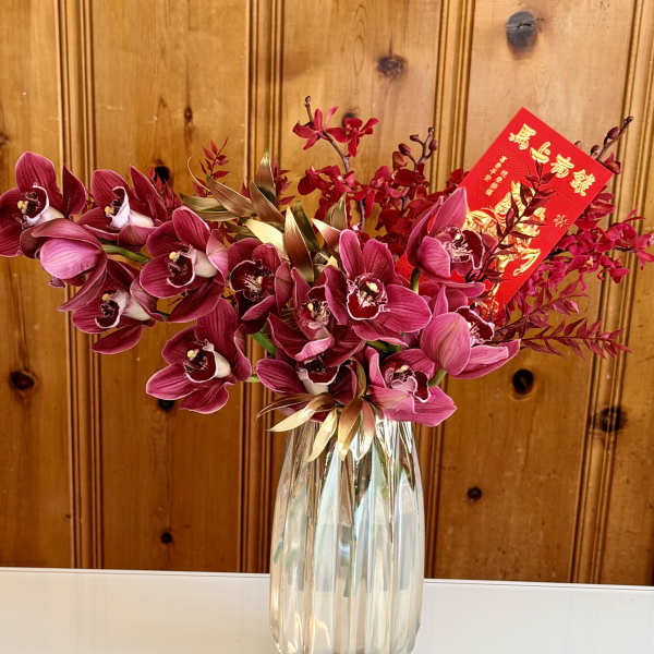 Pink orchids arranged in a clear glass vase with a red envelope card
