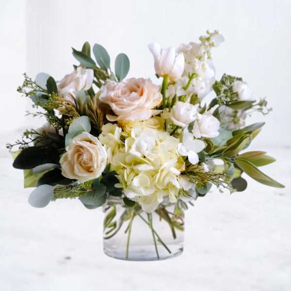 Low glass vase with white hydrangeas, peach roses, and other white flowers in a soft, airy arrangement