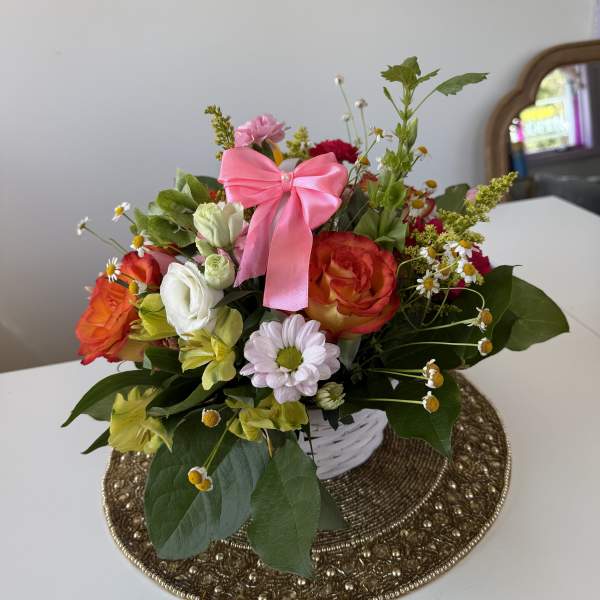 Mixed bouquet of roses, daisies, and alstroemeria in a white basket with a pink bow