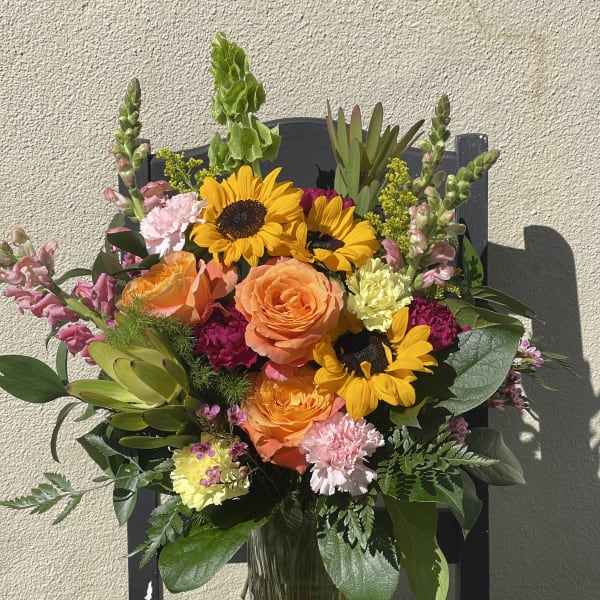 Tall mixed bouquet with sunflowers, orange roses, and pink flowers in a clear glass vase
