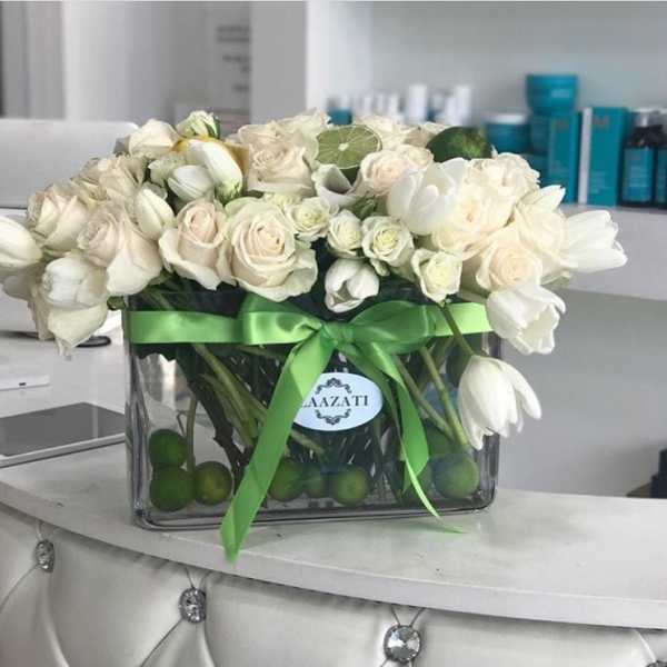White roses and tulips arranged in a glass vase with a green ribbon.