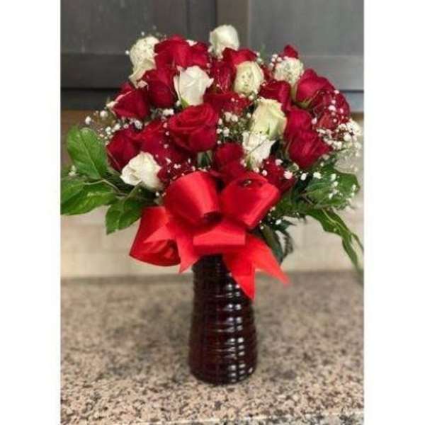 Tall arrangement of red and white roses with baby's breath in a dark vase with a large red bow