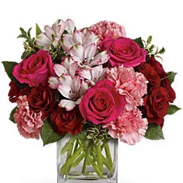 Short arrangement of hot pink and red roses with pink carnations in a clear glass cube vase