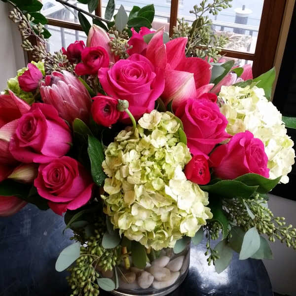 Bouquet of hot pink roses, amaryllis, and pale hydrangeas in a glass vase