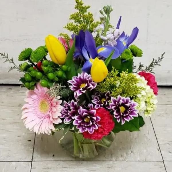 Colorful mixed bouquet with tulips, irises, daisies, and carnations in a glass vase