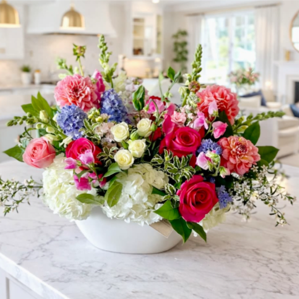 Mixed bouquet of pink, white, blue, and coral flowers in a white bowl vase