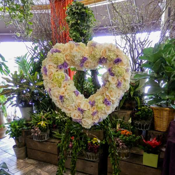 Heart-shaped floral wreath of cream and lavender blooms on a stand