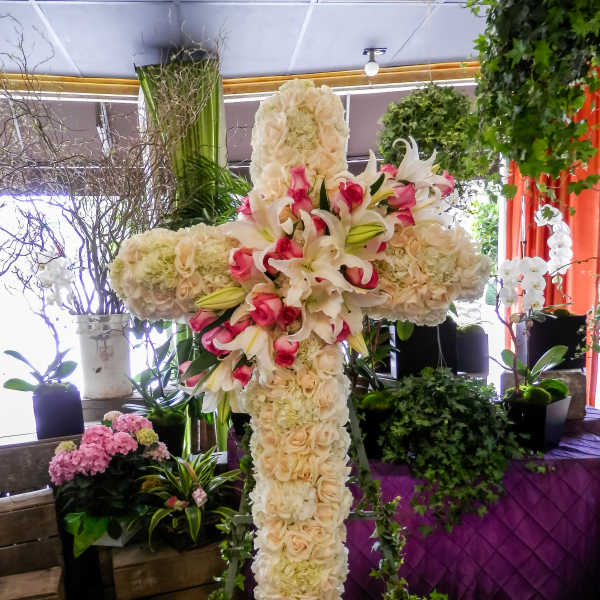 Large floral cross on an easel with white lilies, roses, and pink accents