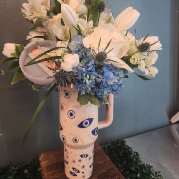 Tall arrangement of white and blue flowers in an evil-eye patterned ceramic tumbler