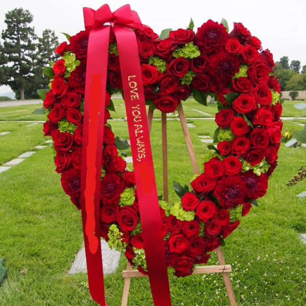 Heart-shaped red rose wreath on an easel with a red ribbon
