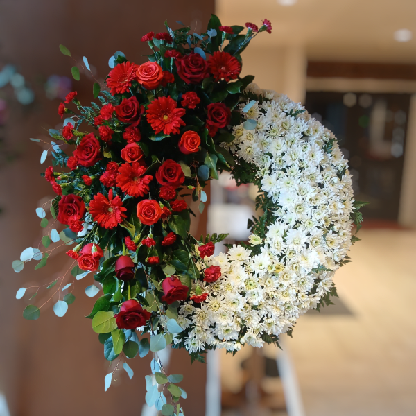 Standing half-red, half-white wreath on an easel with red roses and gerbera daisies.