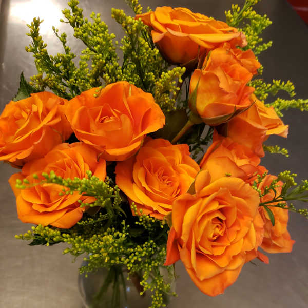 Orange roses arranged in a clear glass vase with green filler flowers