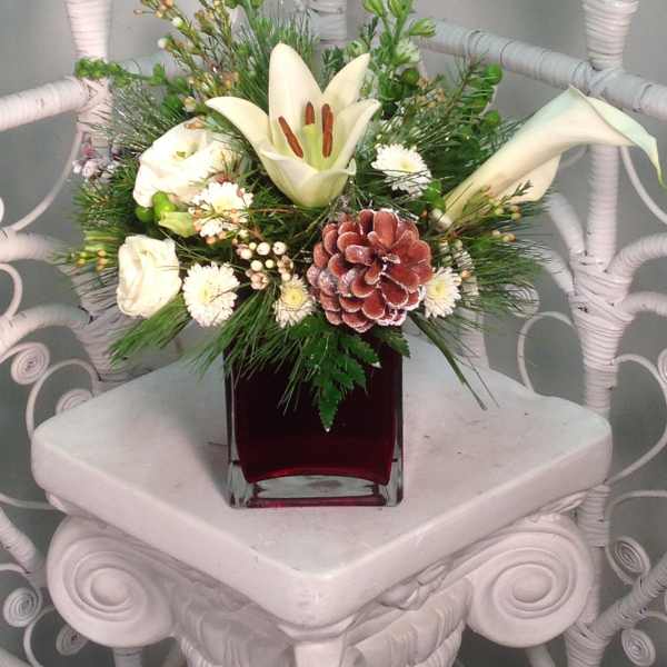White lilies and roses in a red glass vase with pine accents