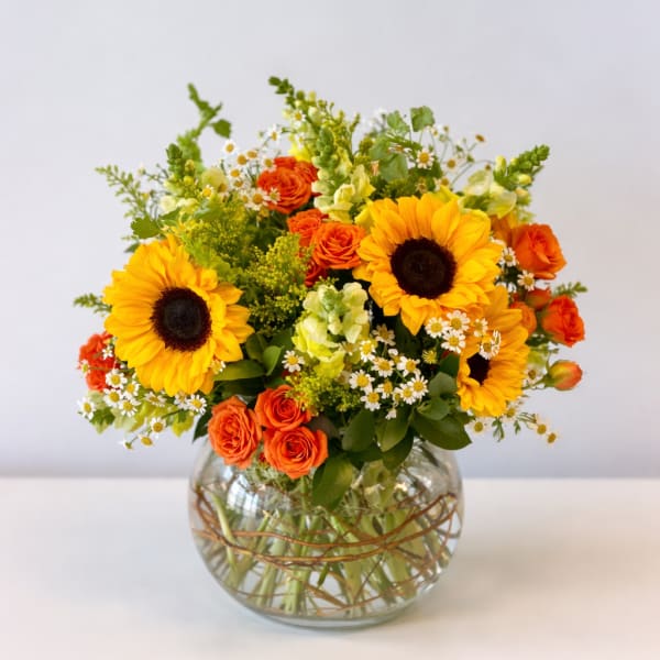 Sunflower and orange rose arrangement in a round glass vase