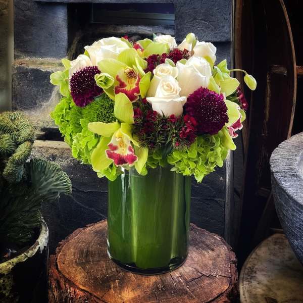 Bouquet of white roses, green orchids, and burgundy blooms in a glass vase