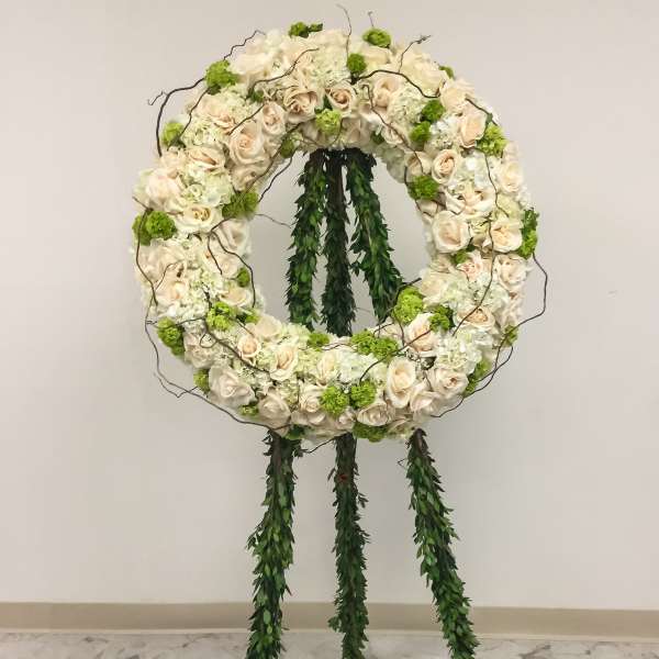 Circular floral wreath on a stand with cream roses and green accents