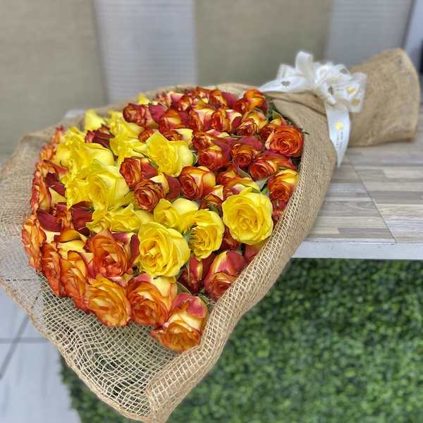 Large bouquet of yellow and orange-red roses wrapped in burlap with a white bow.