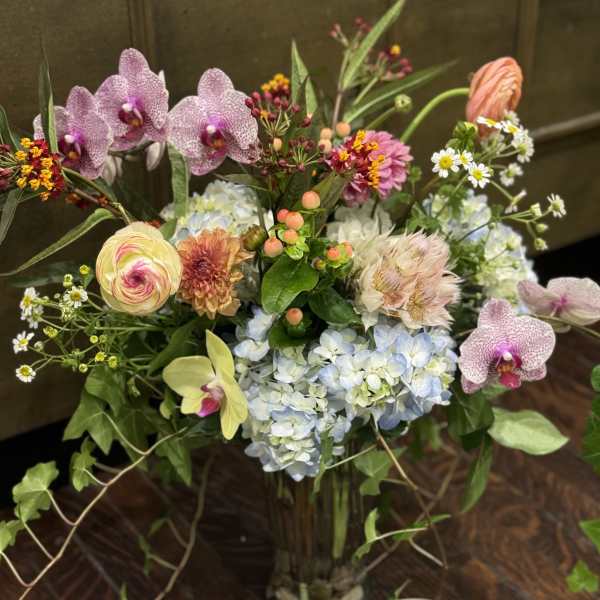 Mixed bouquet with orchids, hydrangeas, and small daisies in a glass vase