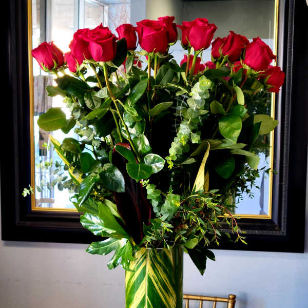 Tall vase arrangement of red roses with mixed greenery