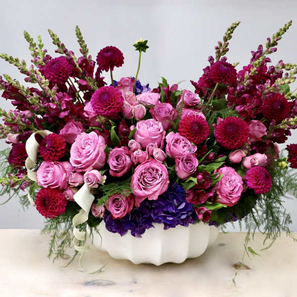 Low pink and magenta arrangement of roses, dahlias, and snapdragons in a white ceramic bowl