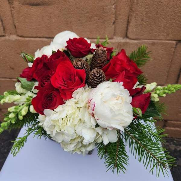 Low arrangement of red roses, white hydrangeas, and pinecones with evergreen in a vase