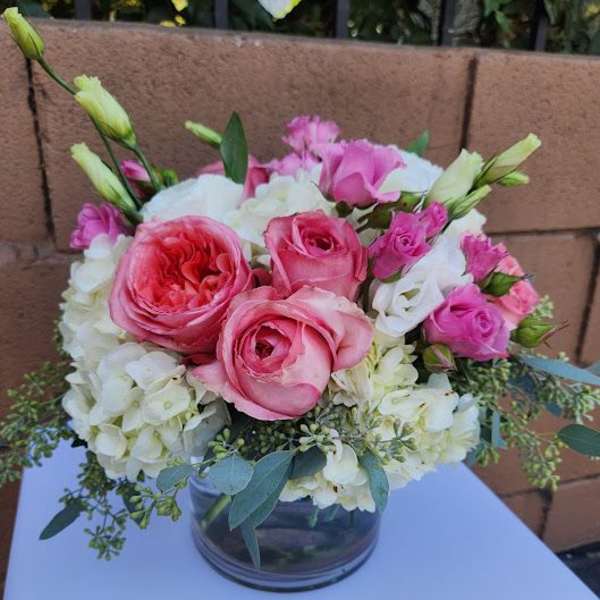 Round arrangement of pink roses, white hydrangeas, and lisianthus in a clear glass vase