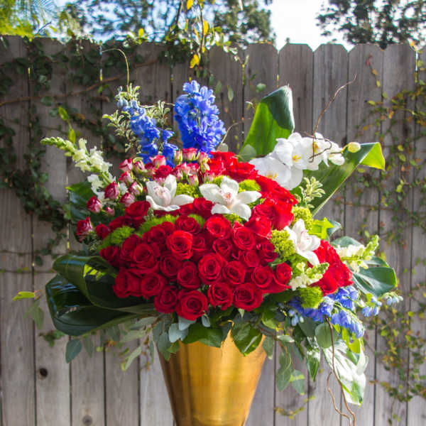 Large red rose arrangement in a gold vase with white and blue flowers