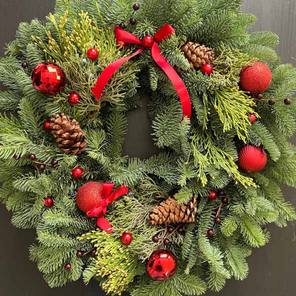 Christmas wreath with evergreen branches, pinecones, red ornaments, and ribbon
