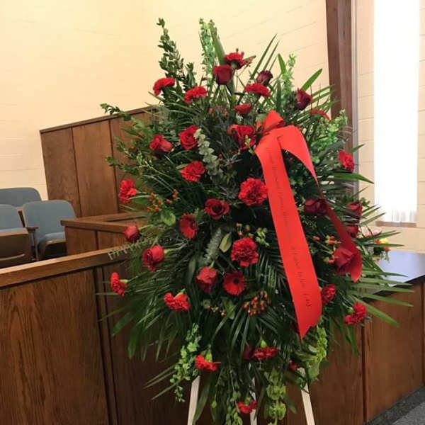 Standing red floral wreath on an easel with a ribbon