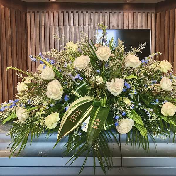 Large white rose and blue flower casket spray on a silver casket
