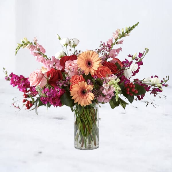 Mixed bouquet of roses, gerbera daisies, and snapdragons in a glass vase