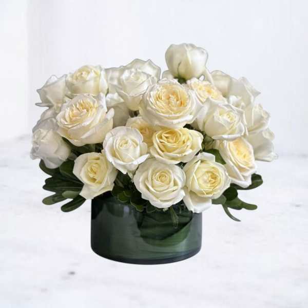 Low arrangement of white and cream roses in a dark green glass cylinder vase