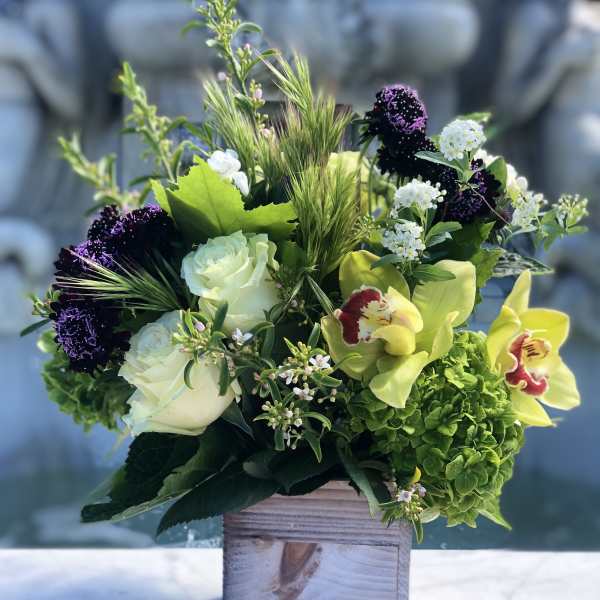 Arrangement of green hydrangea, white roses, and yellow orchids in a rustic wooden cube vase