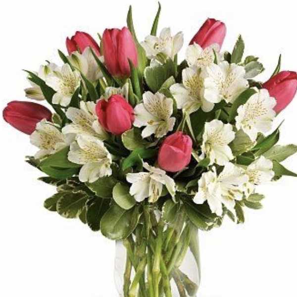 Pink tulips and white flowers arranged in a clear glass vase