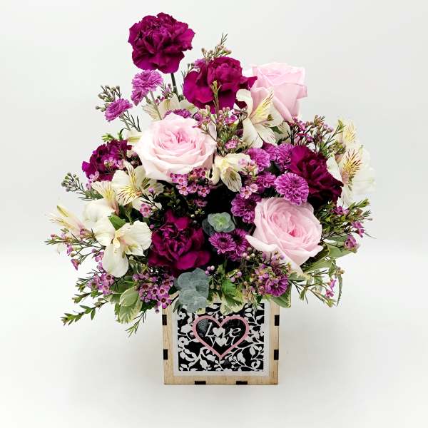 Pink and purple floral arrangement in a wooden box with a heart sign