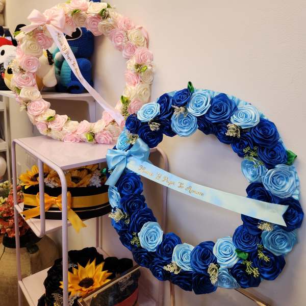Two rose wreaths with satin bows, one pink and one blue