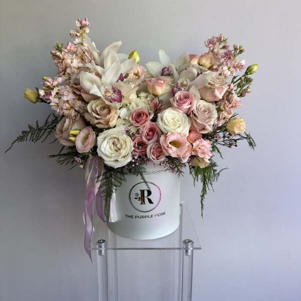 Large pastel pink and white flower arrangement in a white hat box on a clear stand