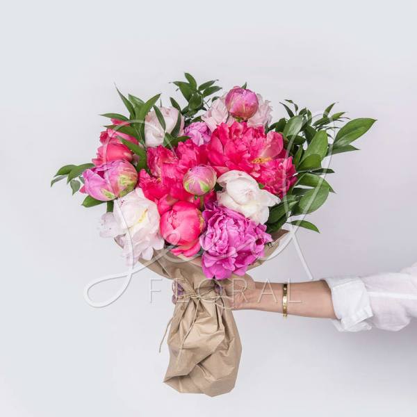 Handheld bouquet of pink and white peonies wrapped in brown paper