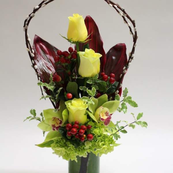 Yellow roses and green orchids in a tall vase with a decorative branch handle