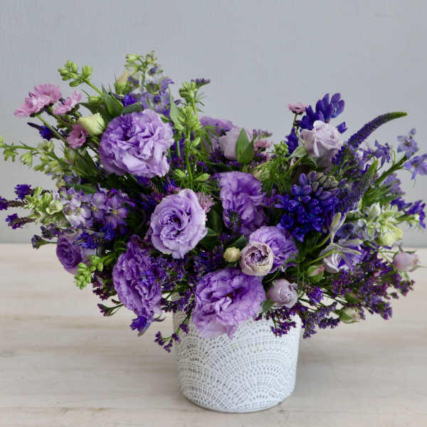 Purple floral arrangement in a white lace-patterned vase