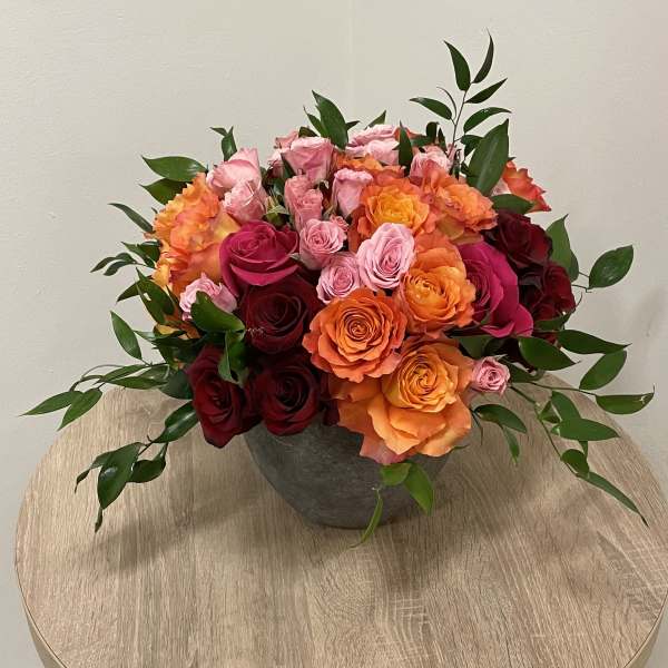 Low arrangement of orange, pink, and red roses in a gray bowl on a wooden table