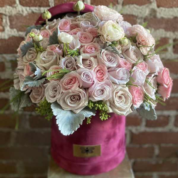 Round arrangement of blush and ivory roses and ranunculus in a pink velvet hatbox.