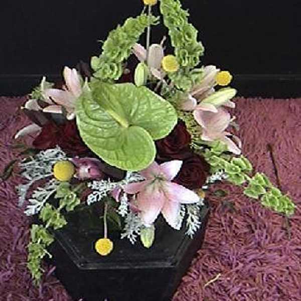Floral arrangement in a black container with pink lilies and green accents