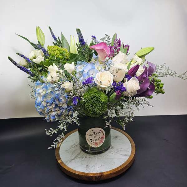 Mixed bouquet in a dark vase with blue hydrangea, white roses, and purple calla lilies