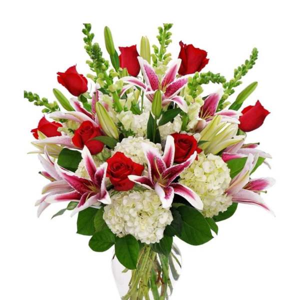 Tall arrangement of red roses, pink lilies, white hydrangeas, and green spikes in a clear glass vase