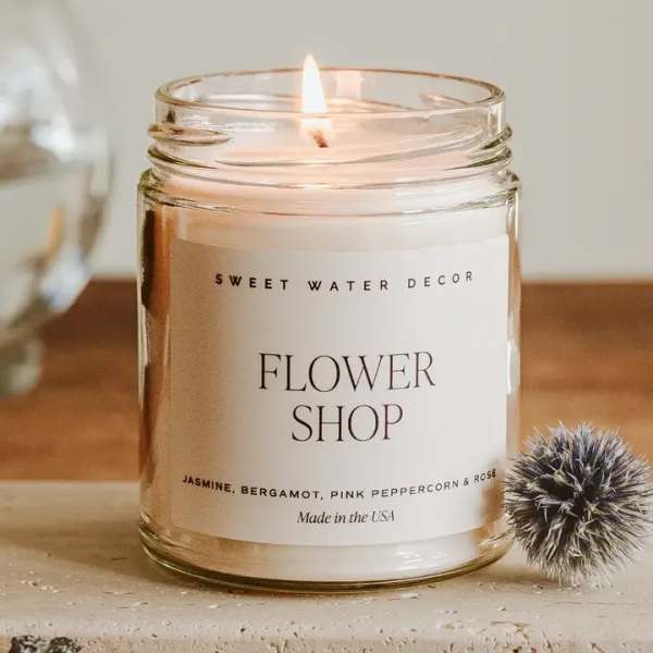 Lit candle in a clear glass jar labeled Flower Shop