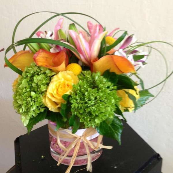 Bouquet of yellow roses, green hydrangeas, and pink lilies in a glass vase