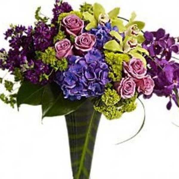 Bouquet of purple roses, blue hydrangeas, and green orchids in a tall vase